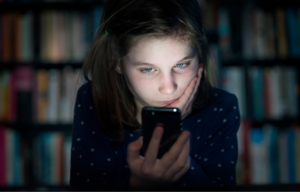 Upset girl looks at phone in dark room